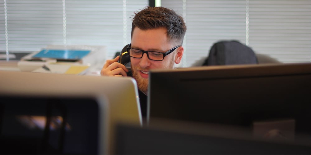 Man on the phone behind two computer screens