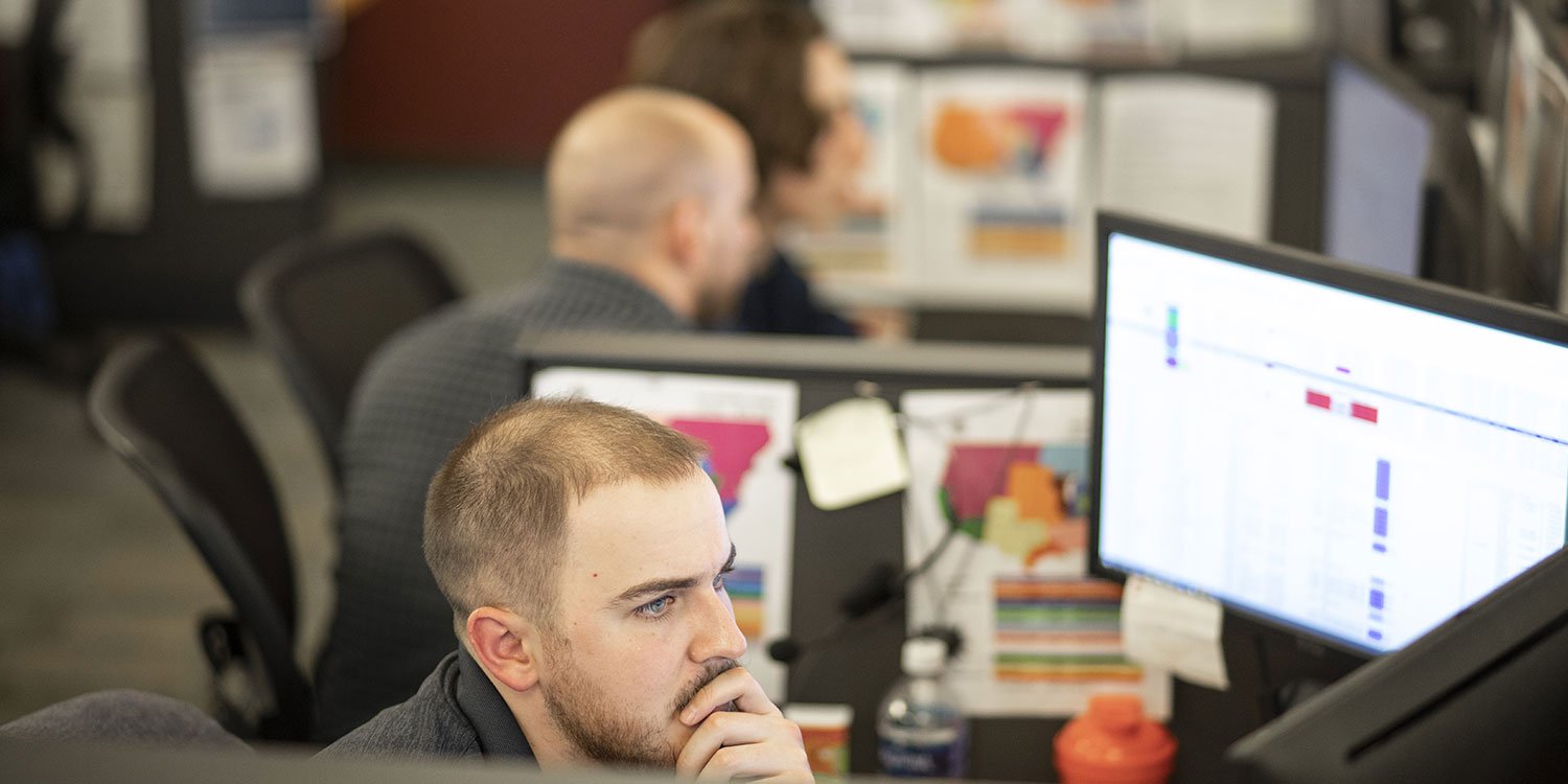 Man looking at computer monitor with two other men viewing monitor in the background