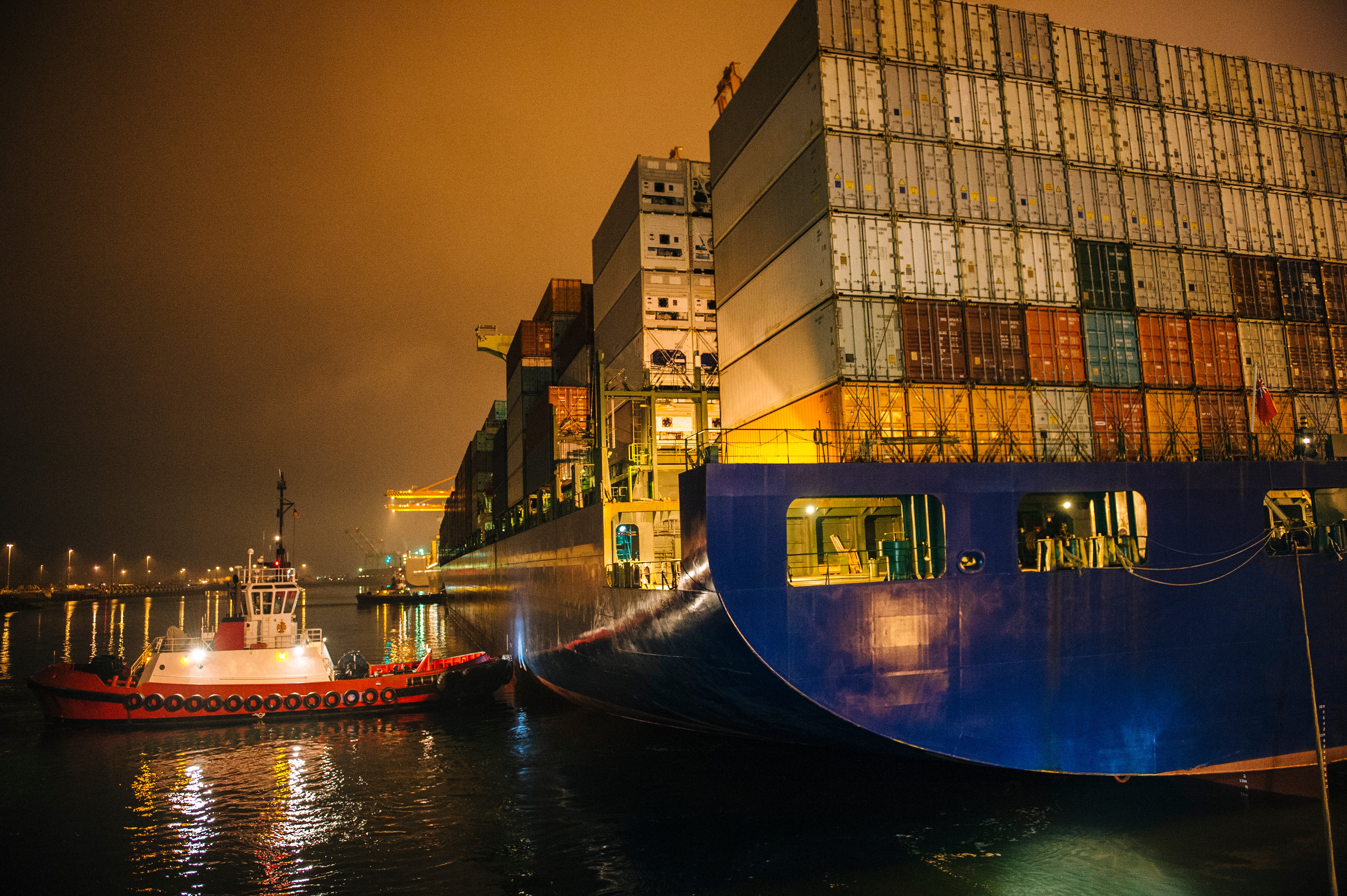 A large containership and a tugboat at a port at night.