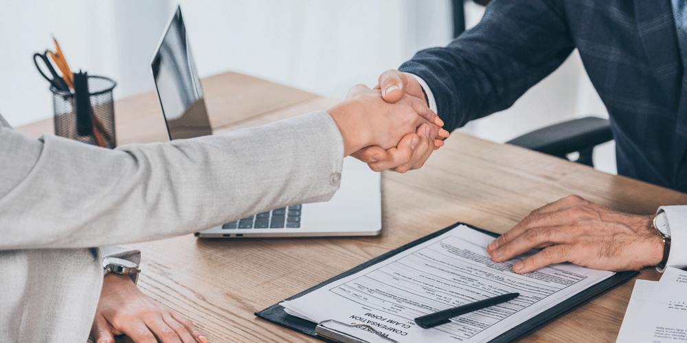 Two individuals shaking hands at a desk.