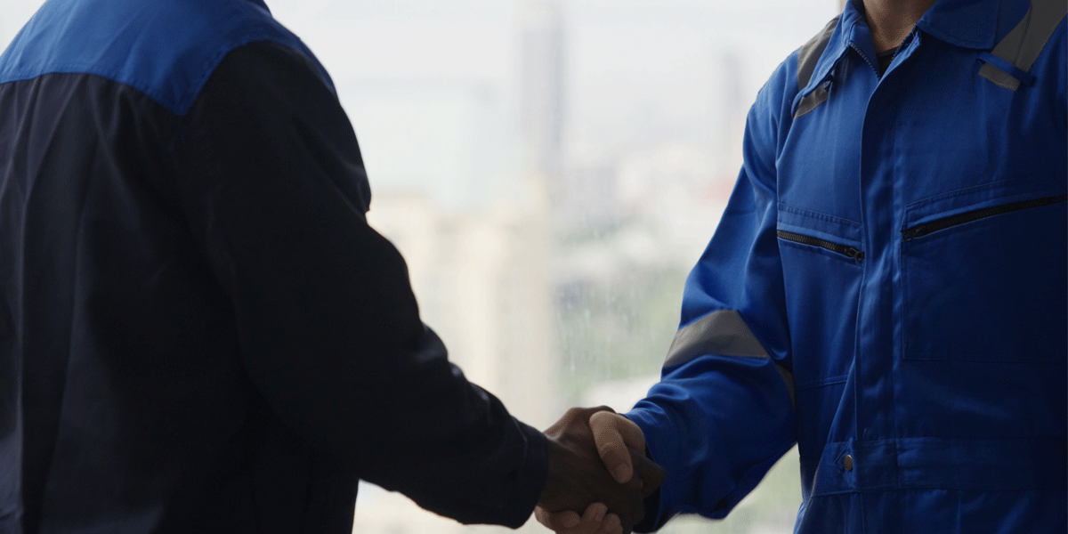 Two people in coveralls shaking hands.