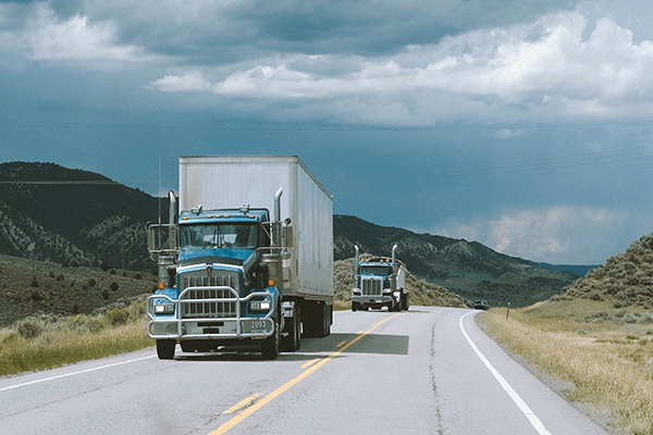 Two dry van trucks traveling on a road through mountains